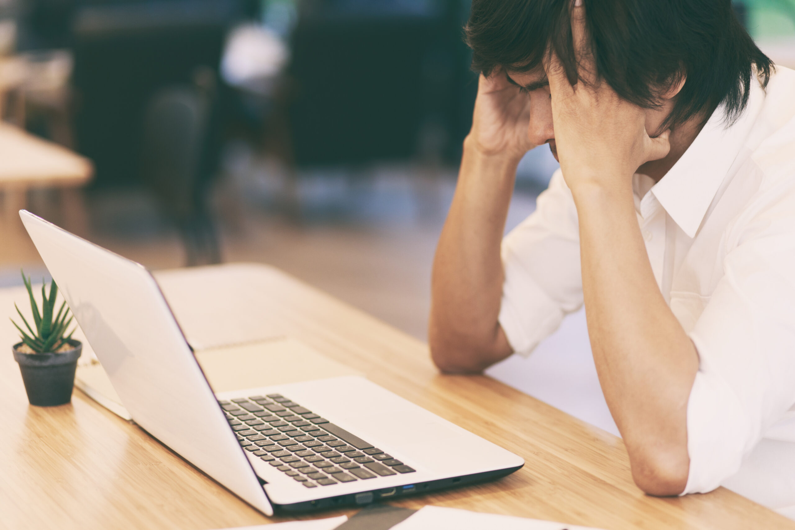 A man sitting with his hands on his head infron tof his laptop, stressed beacuse his e-commerce store isn't generating in to any revenue and he needs e-commerce marketing.