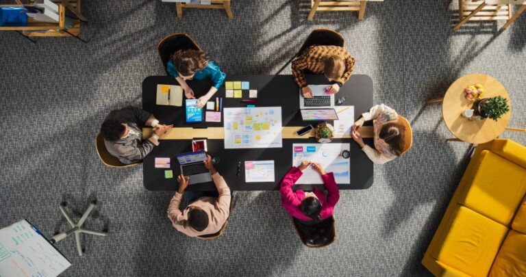 Digital Marketing Agency - Top Down View of Young, Diverse Entrepreneurs in a Colorful Office, Solving Problems and Designing Software, Using laptop, Tablets, and Creative New Project at Conference Table. Productive Teamwork