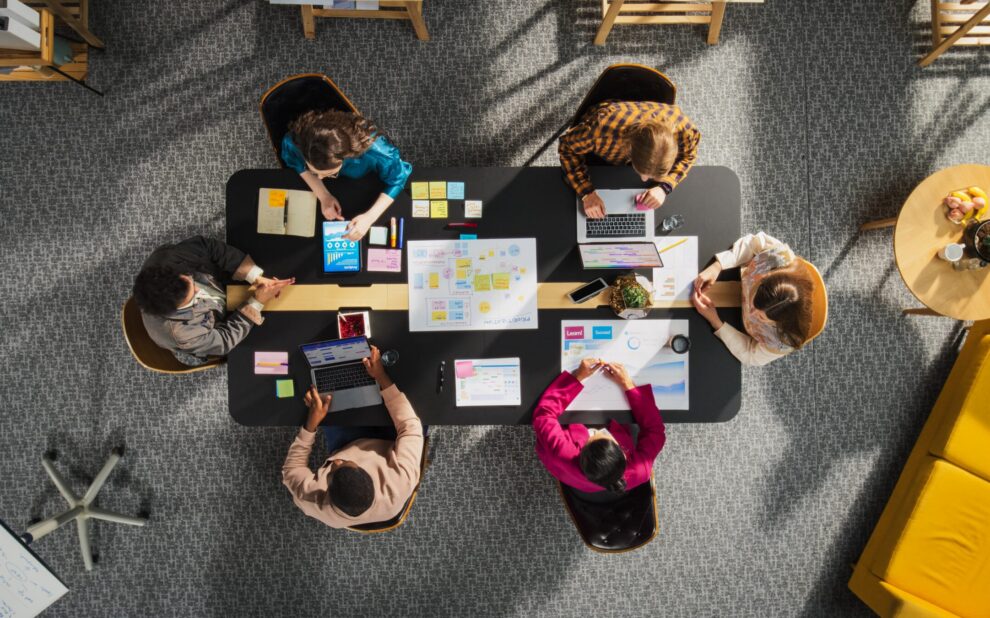 Digital Marketing Agency - Top Down View of Young, Diverse Entrepreneurs in a Colorful Office, Solving Problems and Designing Software, Using laptop, Tablets, and Creative New Project at Conference Table. Productive Teamwork